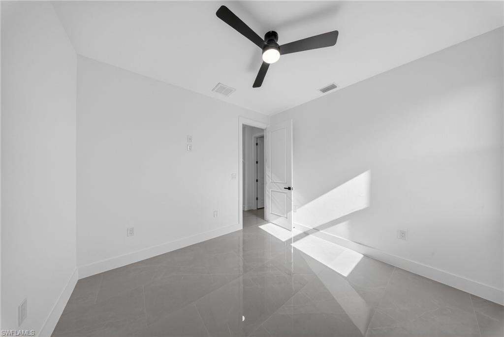 Room featuring large format grey tile flooring, white baseboards, and a black ceiling fan with integrated lighting