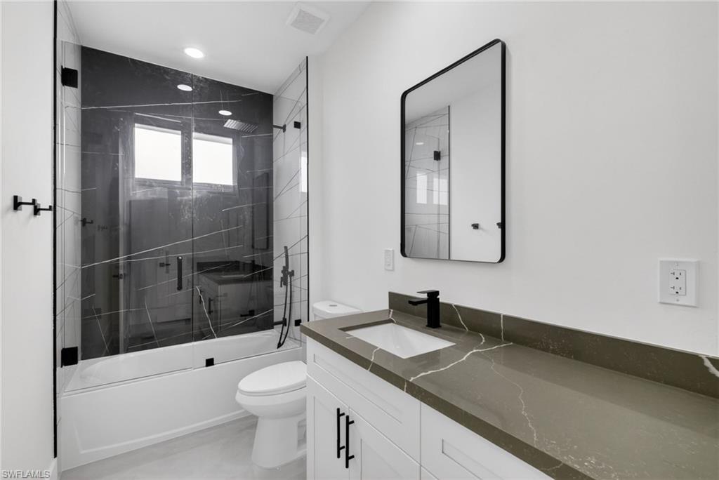 Modern bathroom featuring a glass-enclosed tub and shower combination with black-veined wall tiling