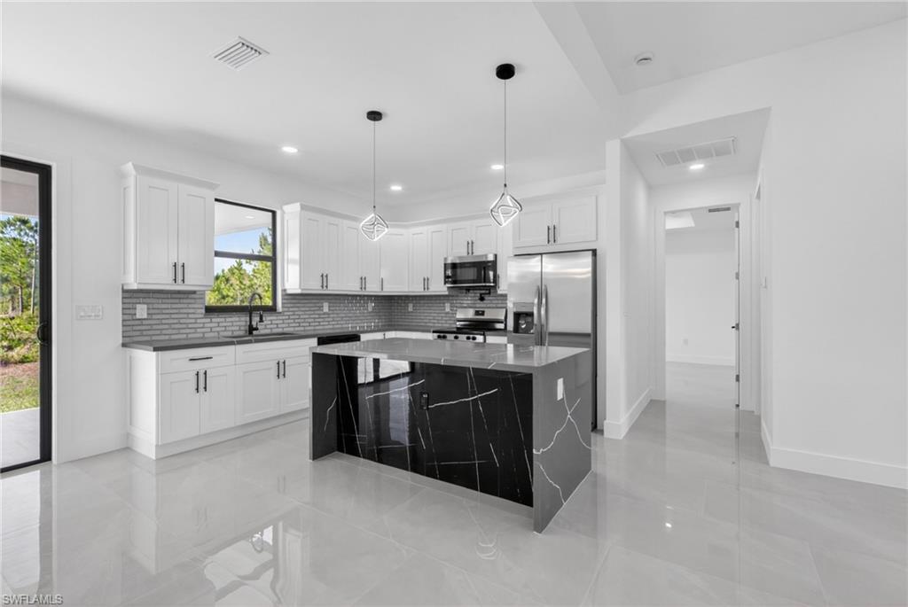 Contemporary kitchen featuring a large black marble island with white veining, white cabinetry, stainless steel appliances, and a gray subway tile backsplash