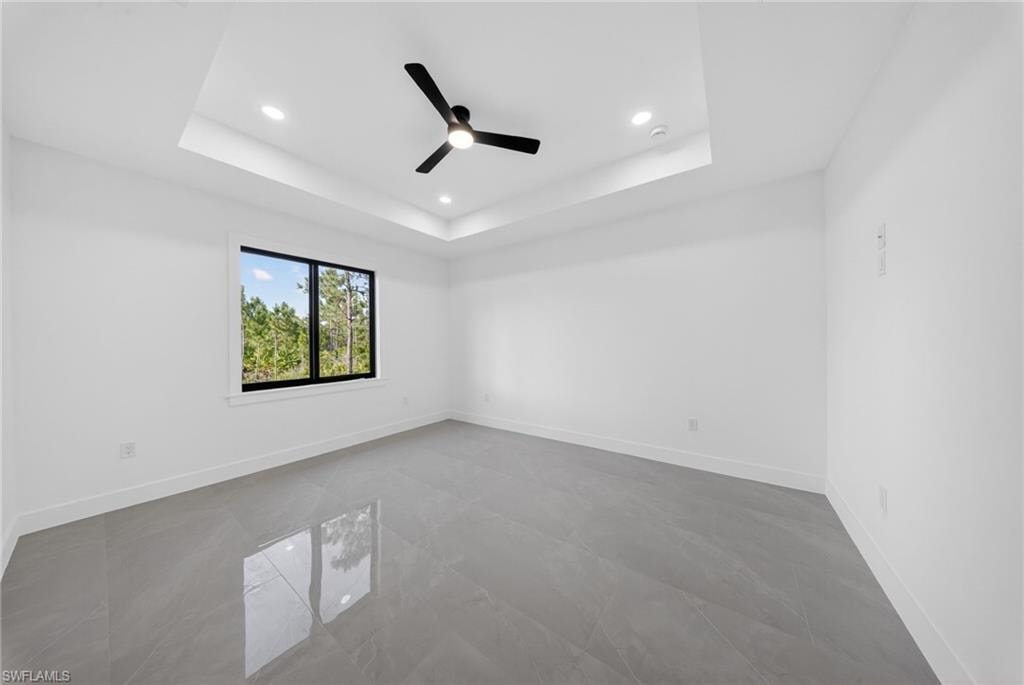 Spacious room featuring a tray ceiling with recessed lighting and a ceiling fan, a large window with black framing, and polished grey tile flooring