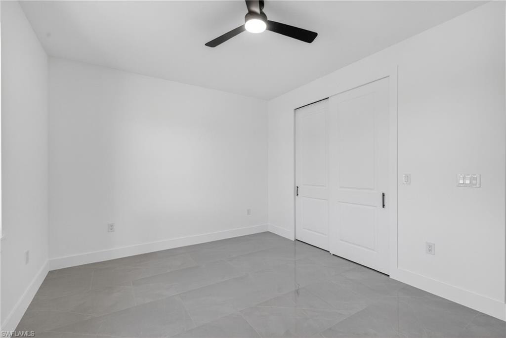 Spacious room featuring modern tile flooring, crisp white walls, a contemporary ceiling fan, and sliding panel closet doors with black hardware