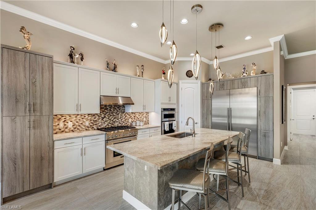 Kitchen featuring under cabinet range hood, white cabinetry, hanging light fixtures, high end appliances, and a center island with sink