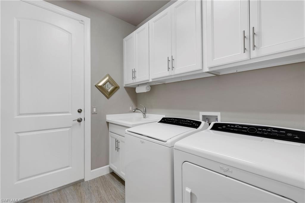 Laundry room with light wood finished floors, washing machine and clothes dryer, cabinet space, a sink, and baseboards