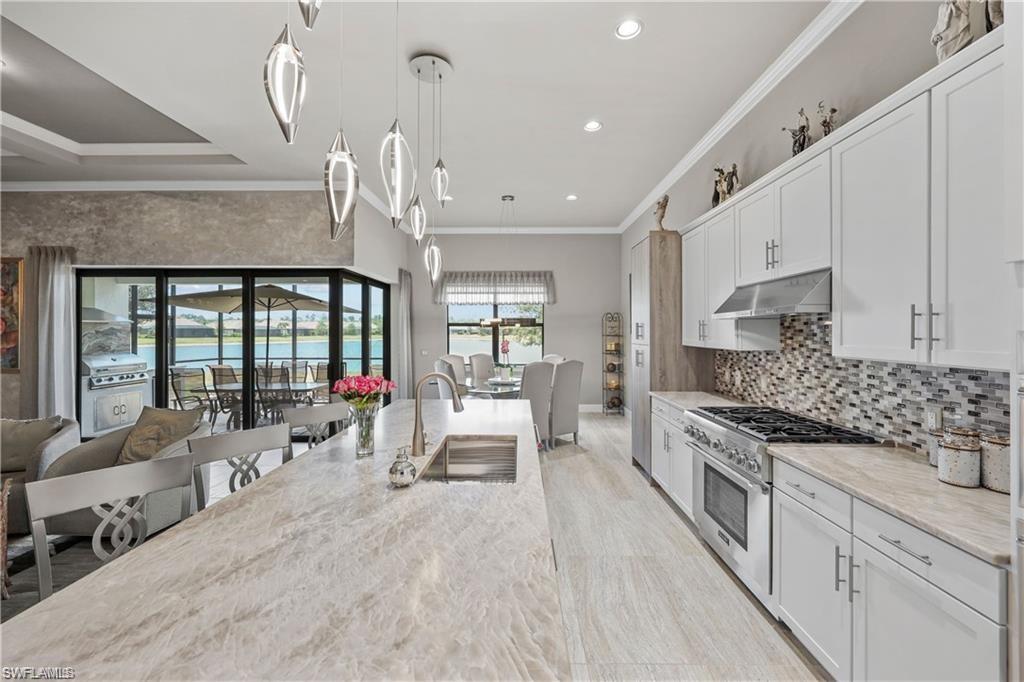 Kitchen featuring stainless steel stove, under cabinet range hood, crown molding, white cabinetry, and pendant lighting