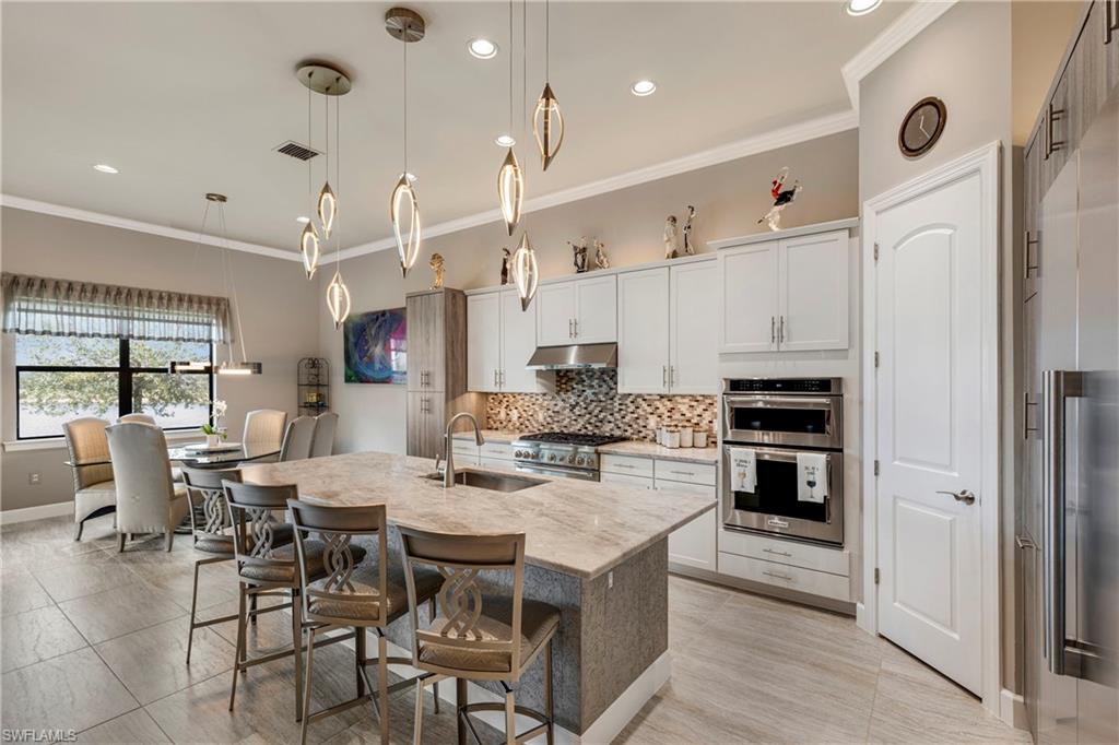 Kitchen with a center island with sink, hanging light fixtures, under cabinet range hood, white cabinetry, and a sink