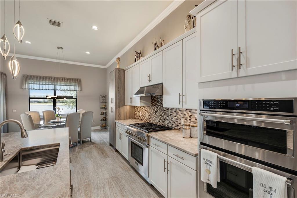 Kitchen featuring decorative light fixtures, stainless steel appliances, white cabinets, a sink, and under cabinet range hood