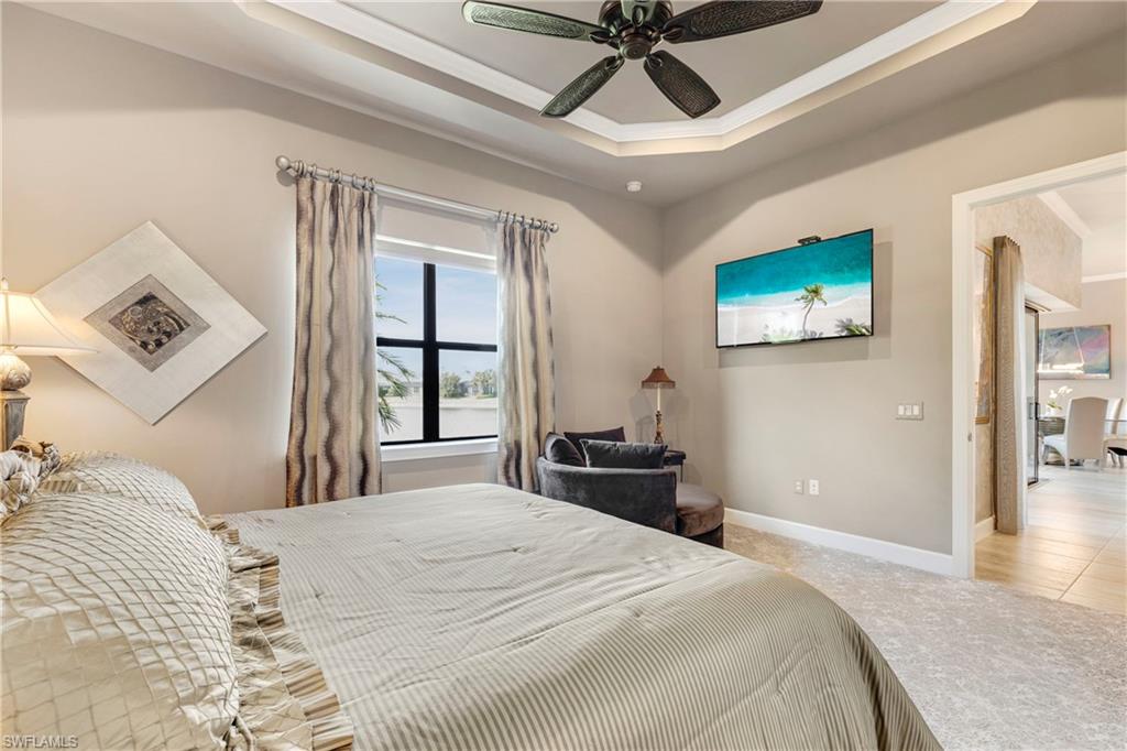 Bedroom with a ceiling fan, a tray ceiling, light colored carpet, and baseboards
