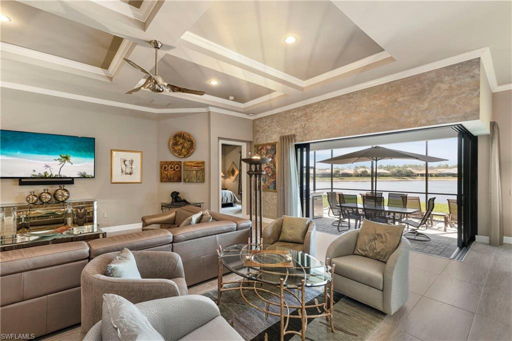 Living room featuring baseboards, coffered ceiling, a ceiling fan, ornamental molding, and a water view