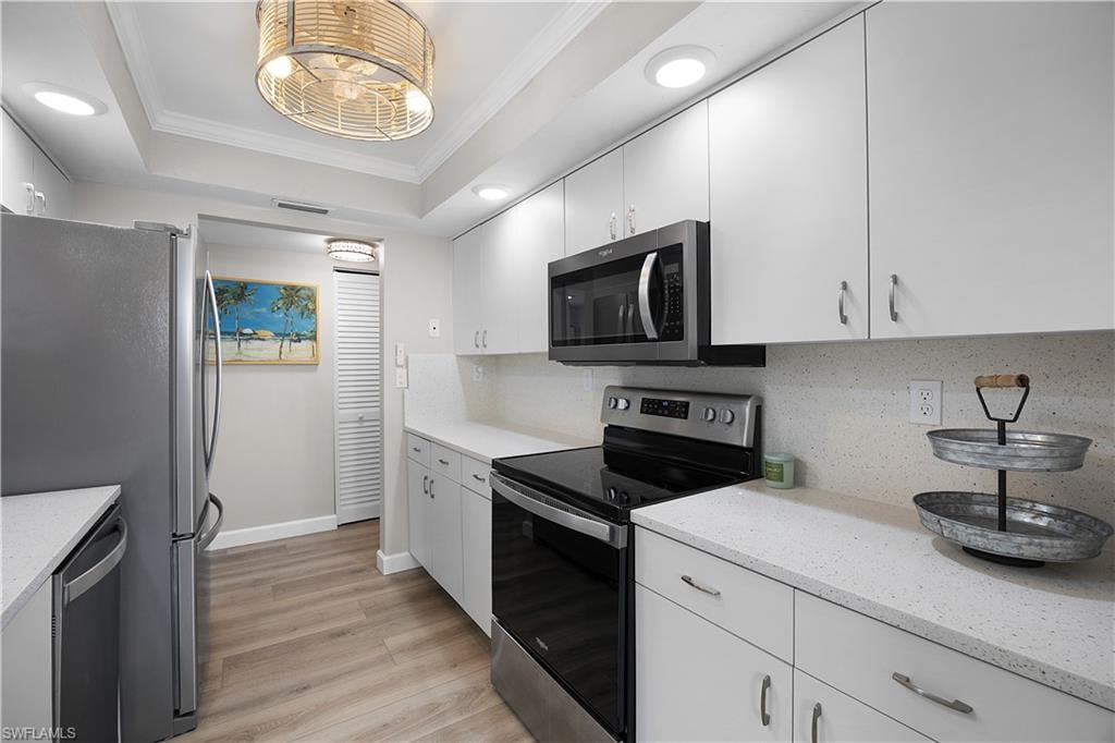Galley kitchen featuring wood-finish flooring, white cabinetry, and stainless steel appliances including a refrigerator, range, and built-in microwave