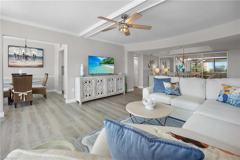Spacious living area featuring light wood-finish flooring, a contemporary ceiling fan, and decorative crown molding