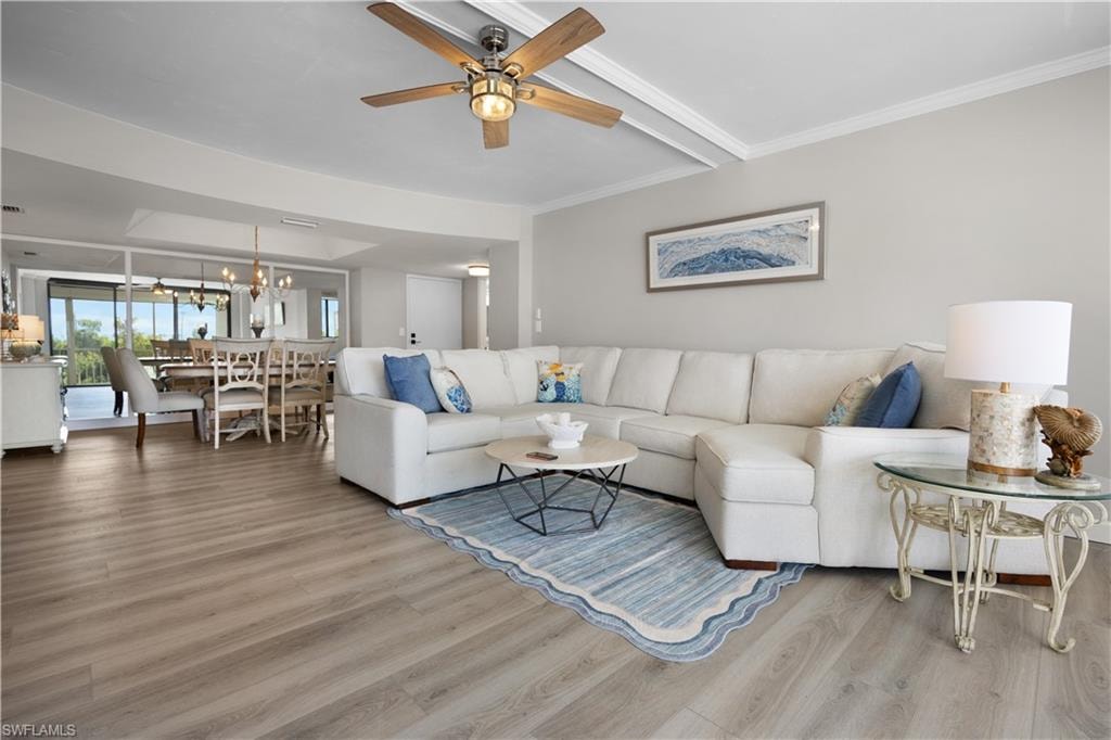 Open-concept living area featuring wood-finish flooring, a ceiling fan with integrated lighting, and a dining area with a chandelier
