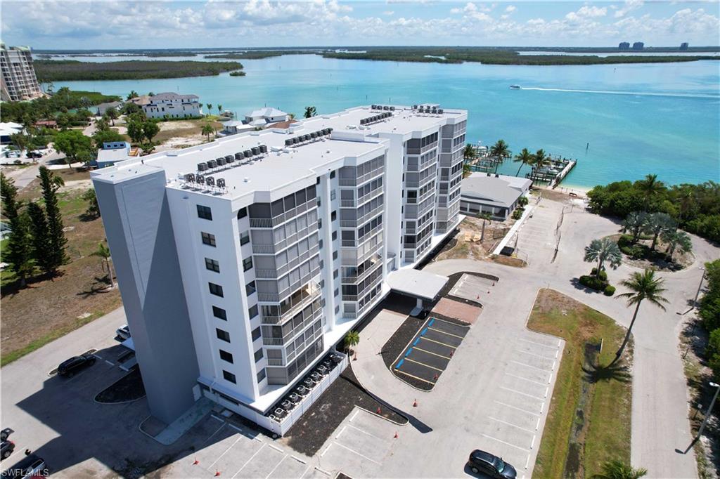 Multi-story residential building featuring a waterside location, extensive parking areas, and mature palm trees