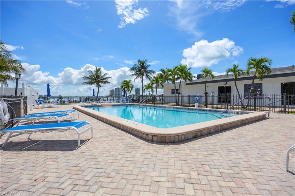 Outdoor swimming pool with a paver deck, surrounded by palm trees and a perimeter fence
