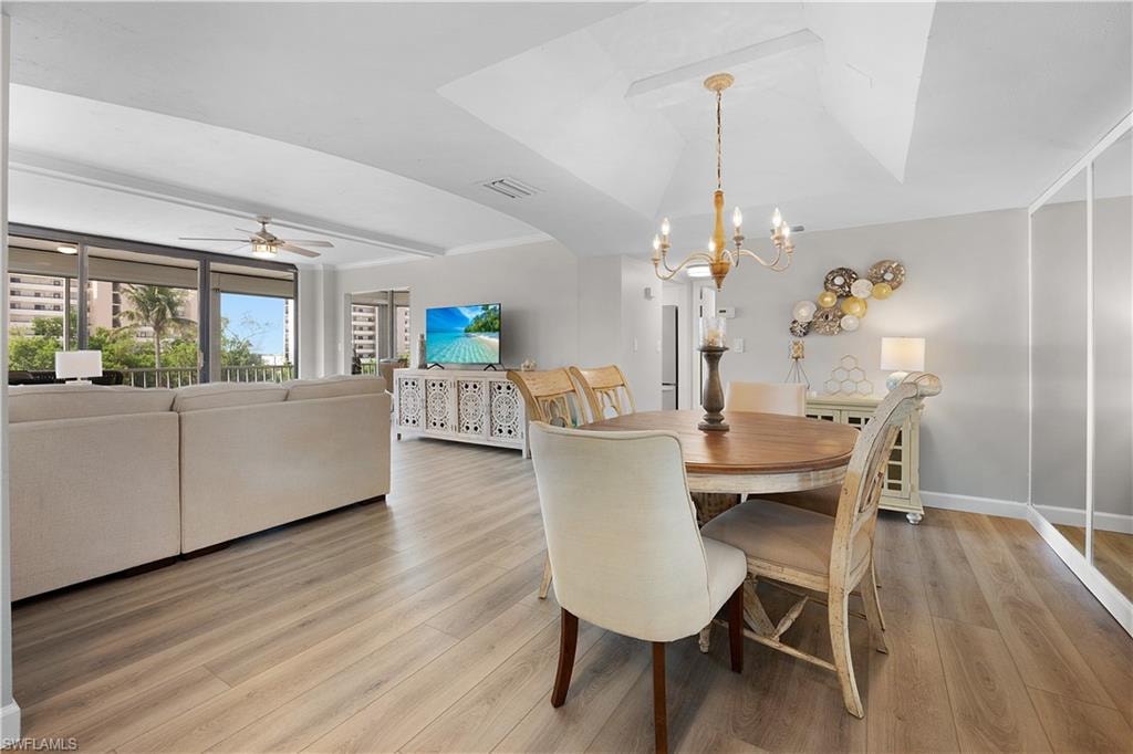 Expansive living and dining areas featuring wood-finish flooring, a tray ceiling with a chandelier, and floor-to-ceiling windows with balcony access