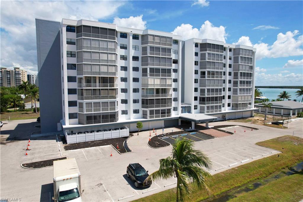 Contemporary multi-story building featuring screened balconies, multiple parking areas, a covered entry, and waterside access