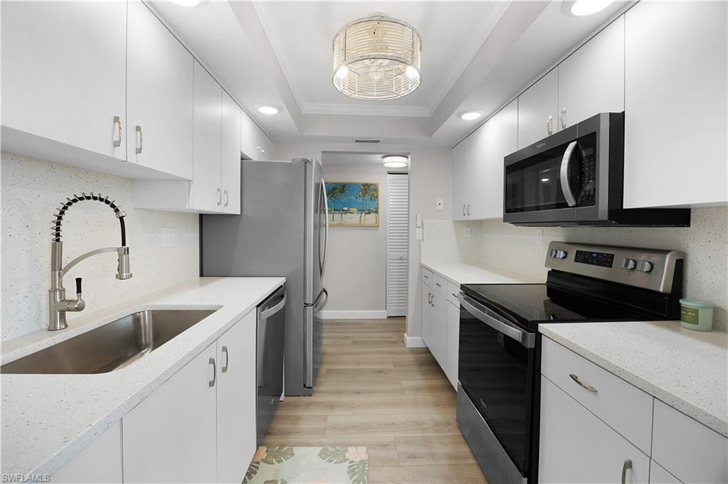 Galley kitchen featuring white cabinetry, light-toned countertops, and wood-finish flooring