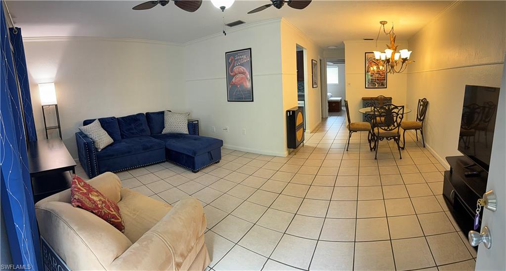 Open-concept living area with tile flooring throughout, featuring crown molding, a ceiling fan, and a chandelier-style light fixture