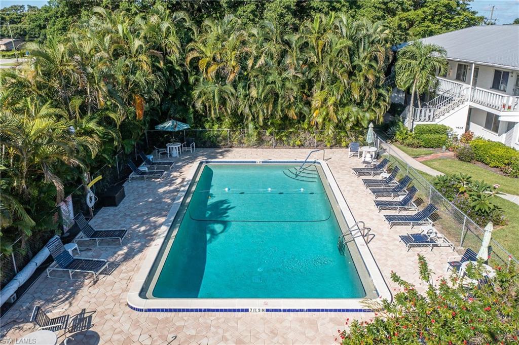 Rectangular swimming pool surrounded by paver patio, featuring a white coping, integrated stairs, and a surrounding chain-link fence