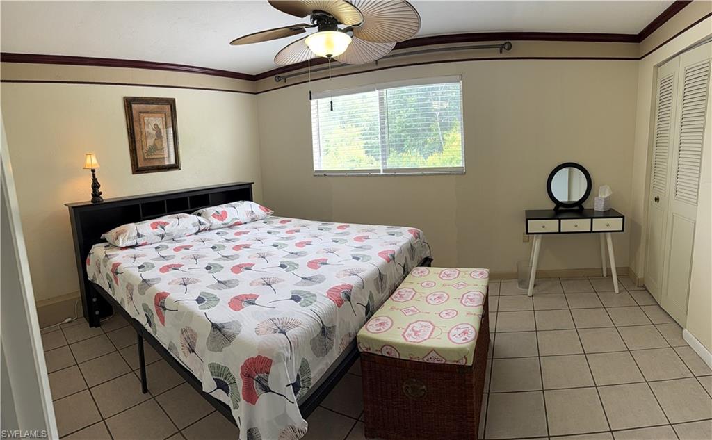 Spacious room featuring neutral-toned walls with decorative trim, a ceiling fan with integrated lighting, a window with blinds, and light-colored tile flooring