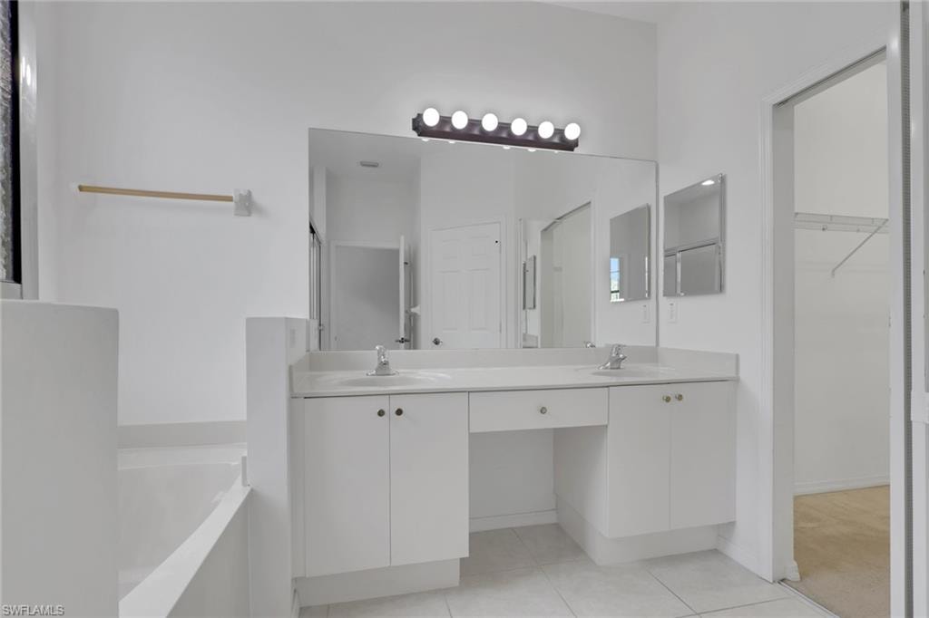 Double vanity with individual sinks, white cabinetry, integrated makeup area, and a large wall-mounted mirror
