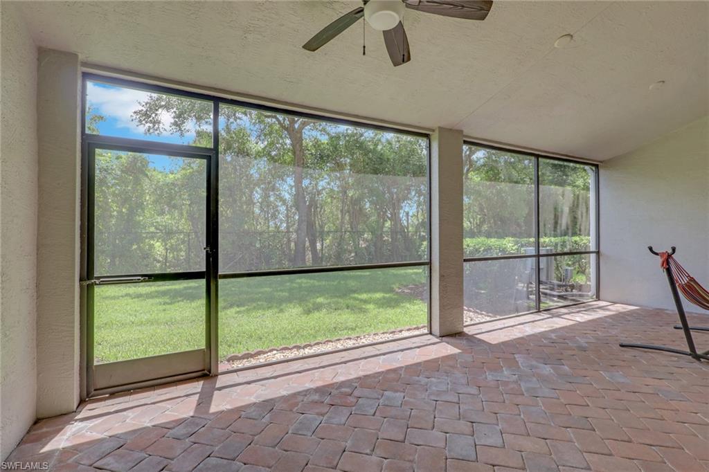 Expansive screened lanai featuring a herringbone-patterned paver floor, a ceiling fan, and direct access to a private backyard