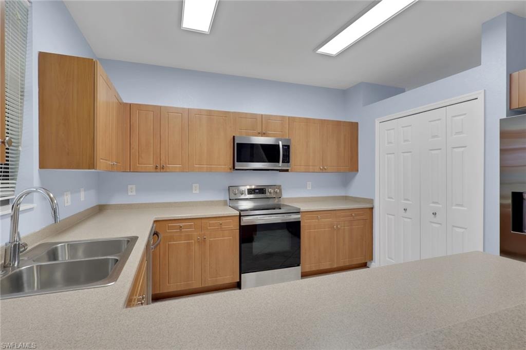 Kitchen featuring wood-finish cabinetry, stainless steel appliances including a range and microwave, light-toned countertops, and a double basin sink.