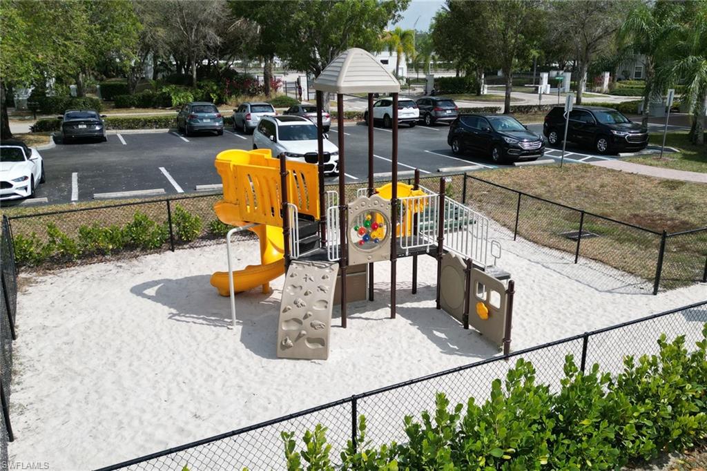 Fenced playground featuring a multi-level structure with slides and climbing elements, set on a sand base