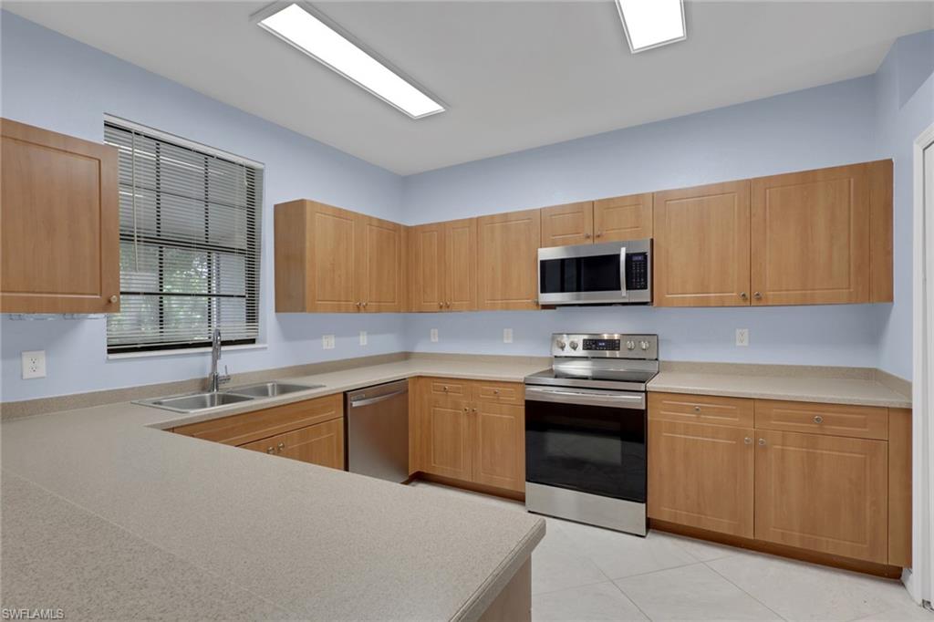 Kitchen featuring light cabinetry, stainless steel appliances, a double basin sink, and ample counter space