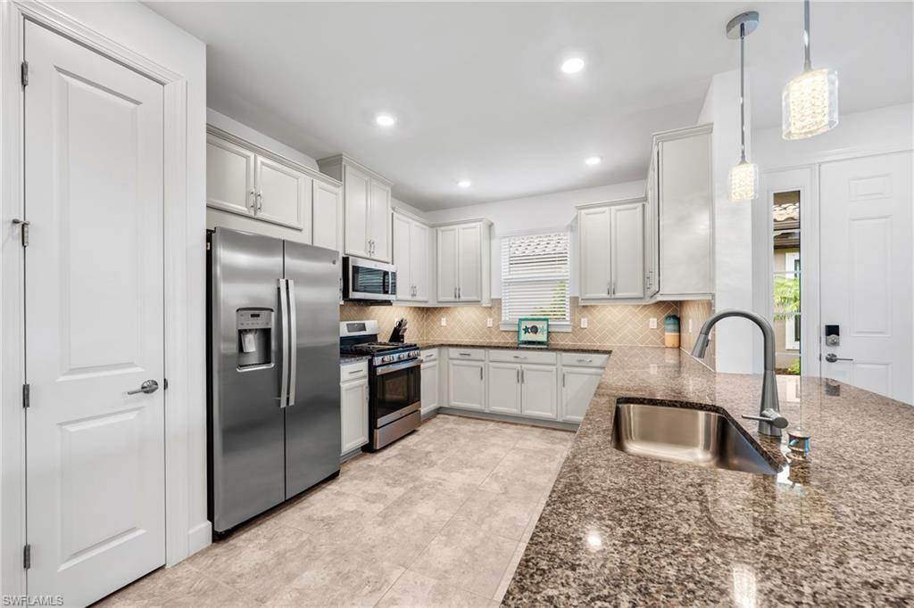 Kitchen featuring white cabinetry, stainless steel appliances, speckled countertops, and a patterned tile backsplash