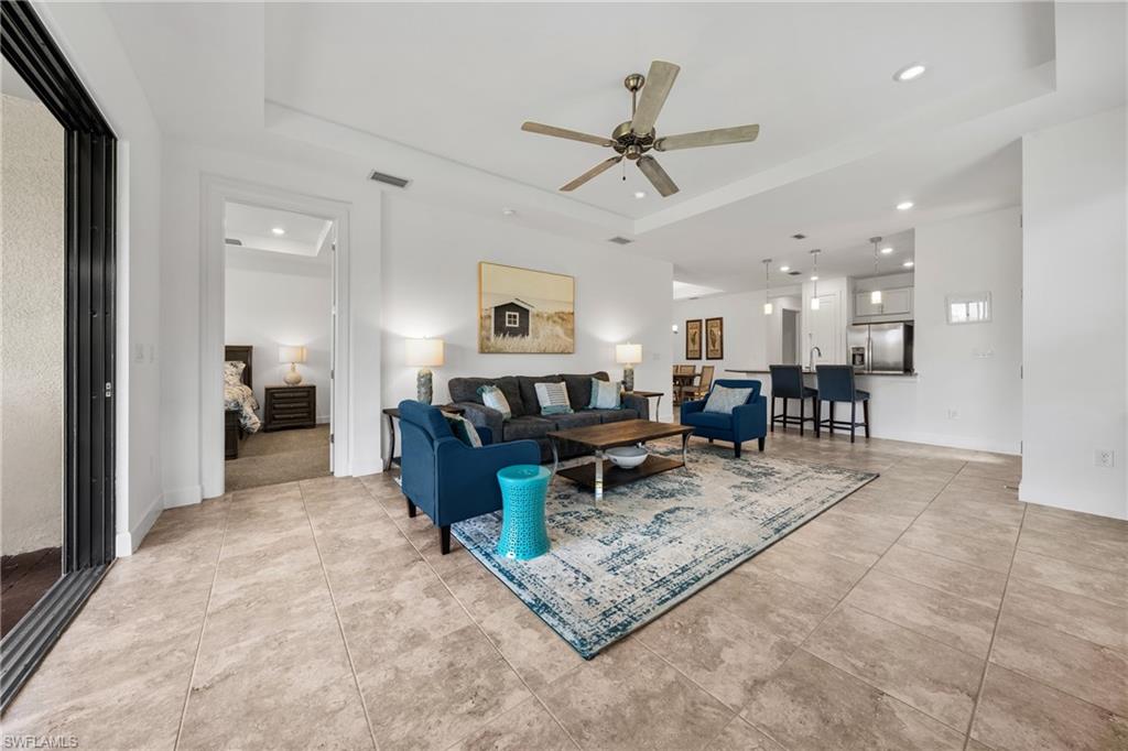 Open-concept living area featuring large format tile flooring, a tray ceiling with a ceiling fan, recessed lighting, and a kitchen with a breakfast bar