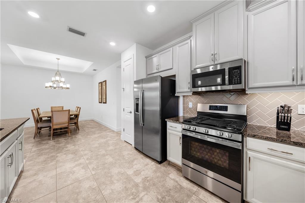 Modern kitchen featuring stainless steel appliances, light cabinetry, granite-style countertops, and a herringbone tile backsplash