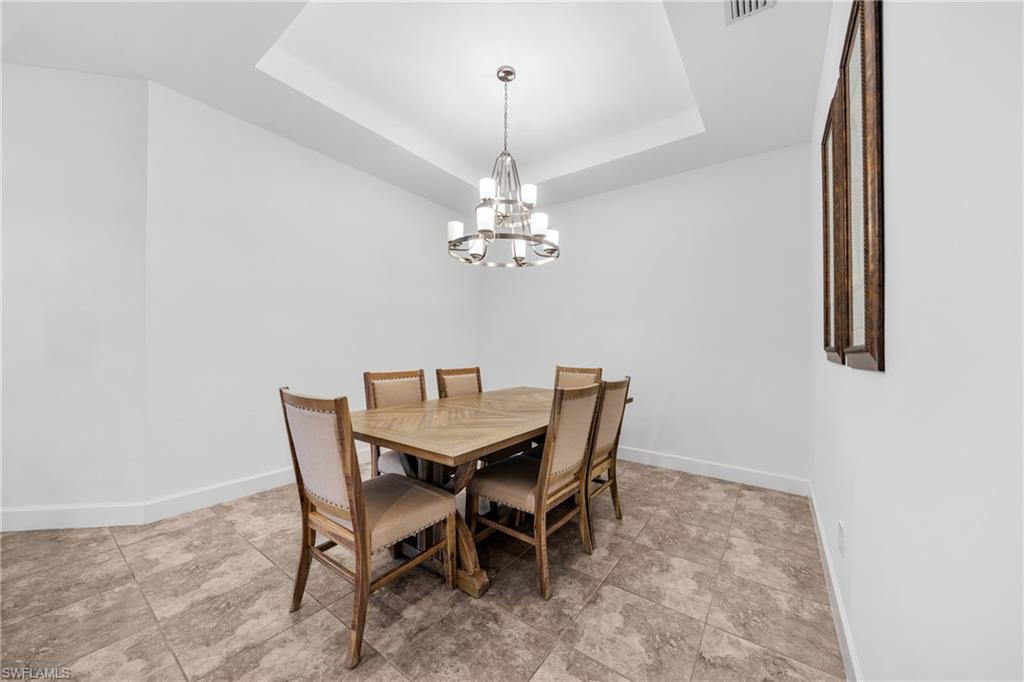 Dining area featuring a tray ceiling with a contemporary chandelier, neutral wall paint, and large format tile flooring
