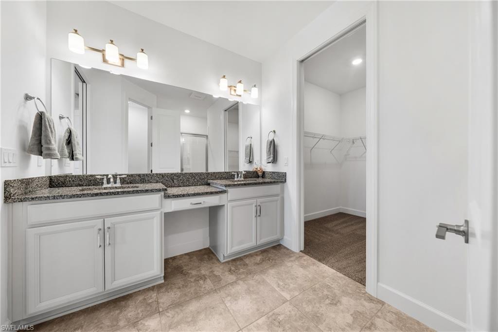 Double vanity featuring granite countertops with undermount sinks and brushed nickel faucets, white cabinetry, and a full-width mirror