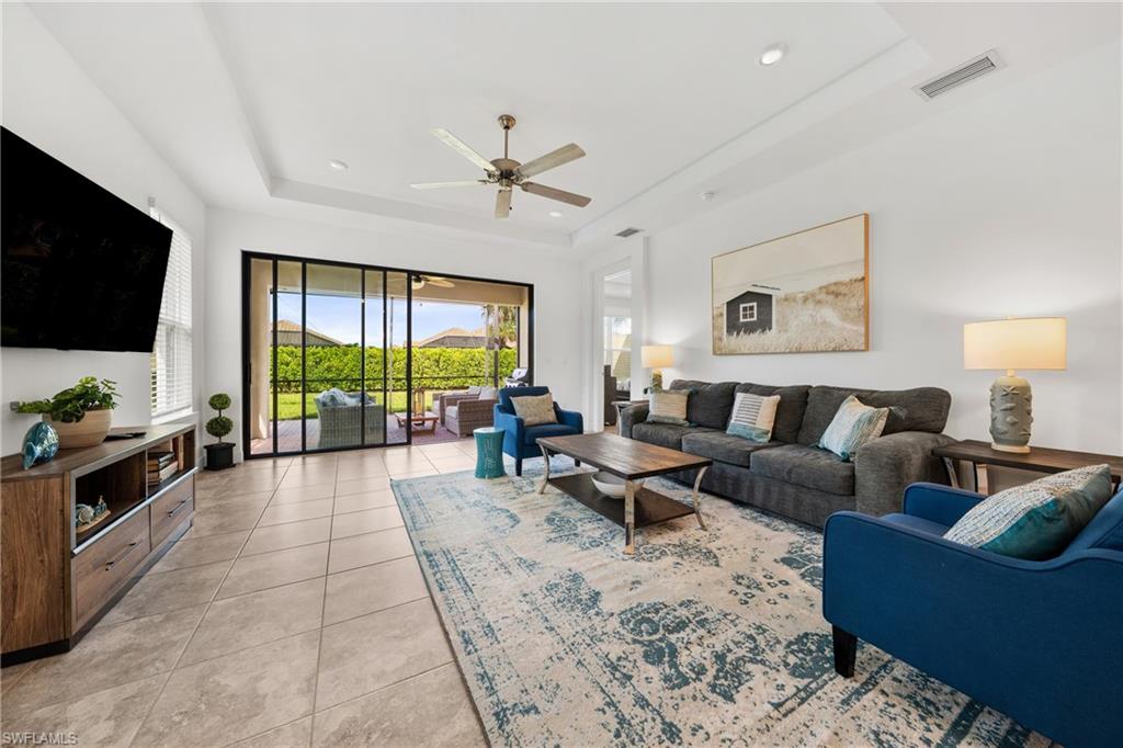 Open-concept living area featuring tile flooring, a tray ceiling with a ceiling fan, and recessed lighting