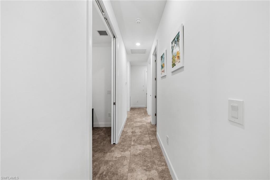 Hallway featuring neutral-toned tile flooring, recessed ceiling lighting, and crisp white walls