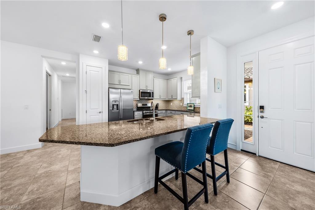 Kitchen featuring light cabinetry, stainless steel appliances, a multi-toned countertop island, and recessed lighting
