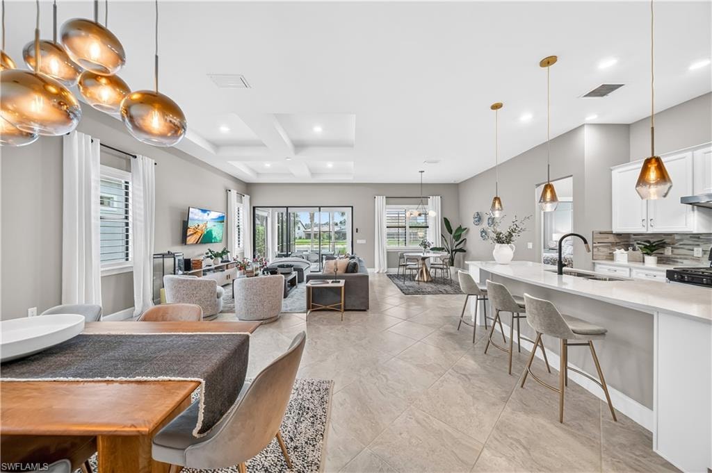 Open-concept living space featuring large format tile flooring, a kitchen island with seating, pendant lighting, recessed ceiling details, and expansive sliding glass doors