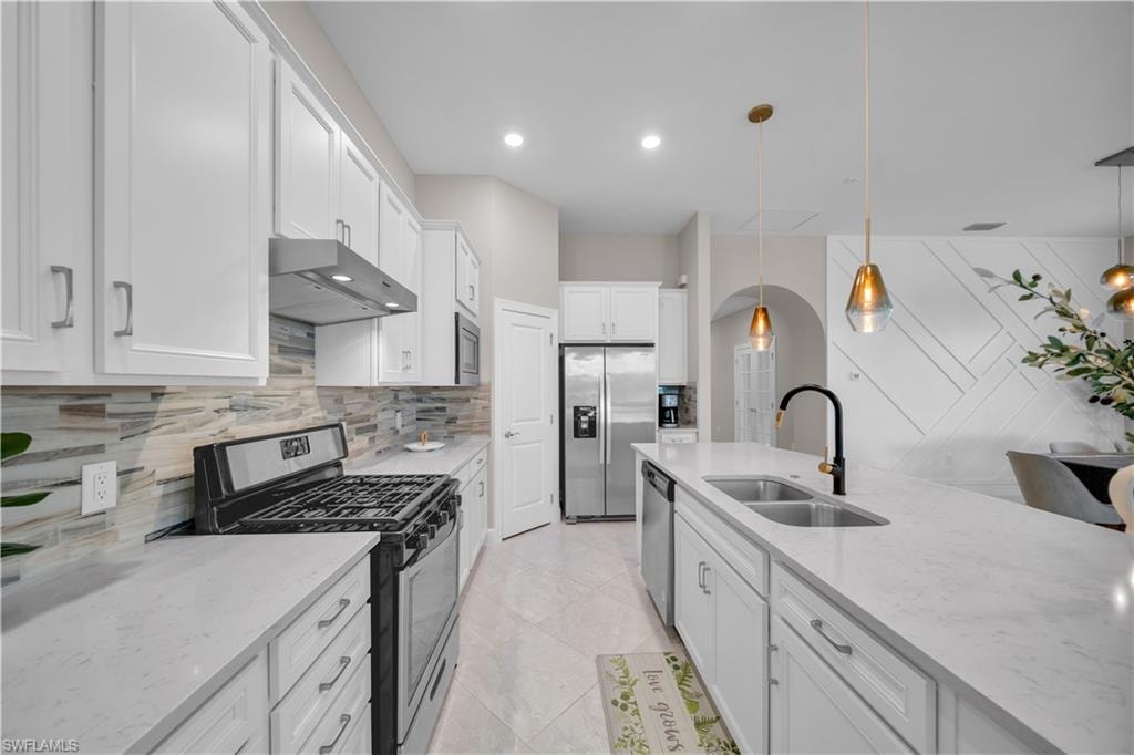 Modern kitchen featuring a gas range, stainless steel appliances, white cabinetry with brushed nickel hardware, and a center island with double sink and pendant lighting