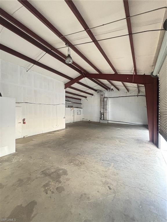 Expansive open warehouse space with a concrete floor, exposed steel beam ceiling structure, and a large roll-up door