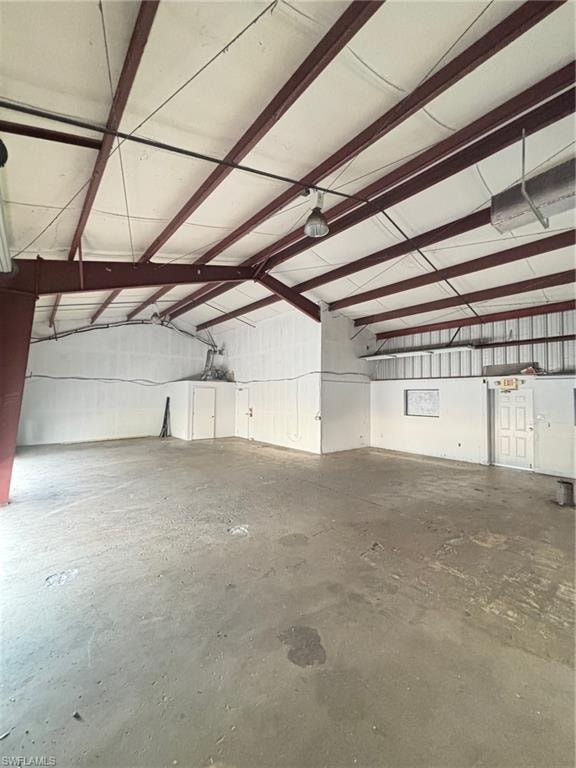 Spacious commercial interior featuring a concrete floor, exposed metal beam ceiling structure, and multiple wall-mounted light fixtures