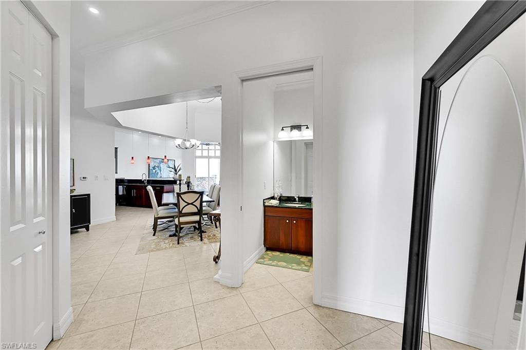 Hall with a chandelier, light tile patterned floors, baseboards, ornamental molding, and a sink