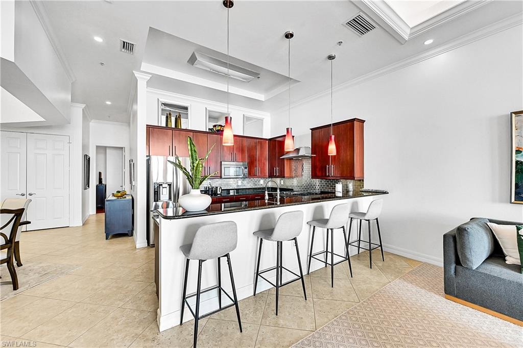 Kitchen featuring wall chimney range hood, dark brown cabinets, stainless steel appliances, dark countertops, and ornamental molding