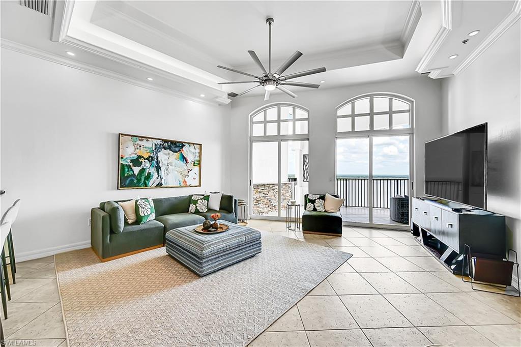 Living area featuring a tray ceiling, ornamental molding, recessed lighting, light tile patterned floors, and ceiling fan
