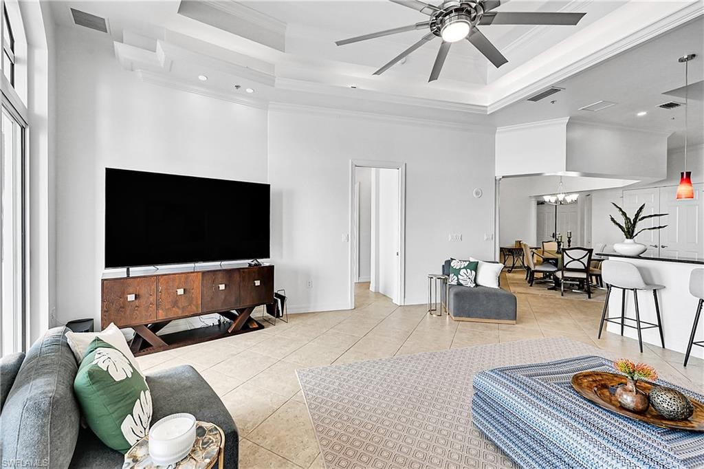 Living room featuring a raised ceiling, light tile patterned floors, a towering ceiling, ornamental molding, and ceiling fan