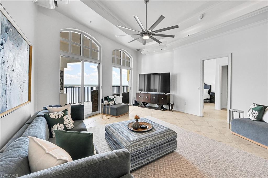Tiled living area featuring ornamental molding, a ceiling fan, a towering ceiling, a tray ceiling, and baseboards