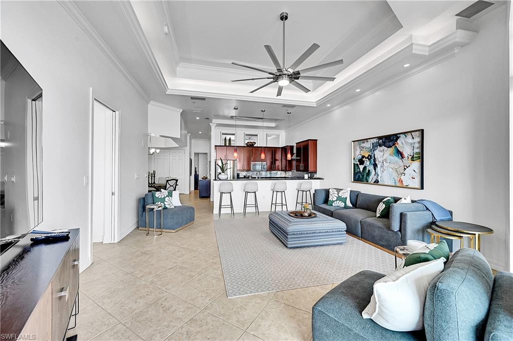 Living room with a ceiling fan, crown molding, a raised ceiling, light tile patterned floors, and recessed lighting