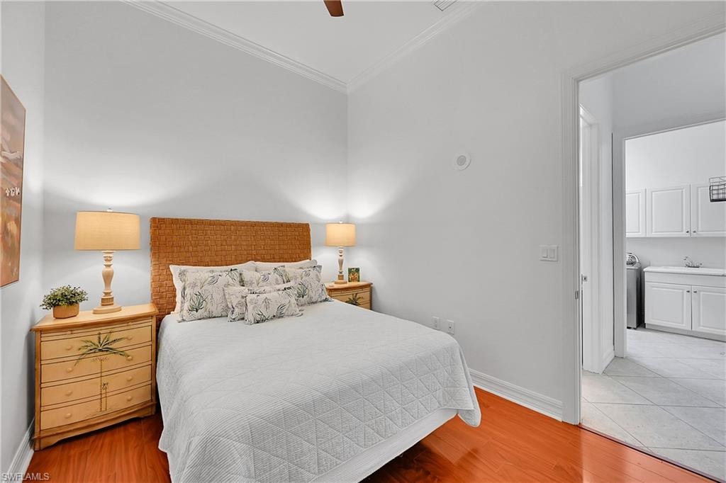 Bedroom with ornamental molding, light wood-style flooring, baseboards, ensuite bath, and a ceiling fan