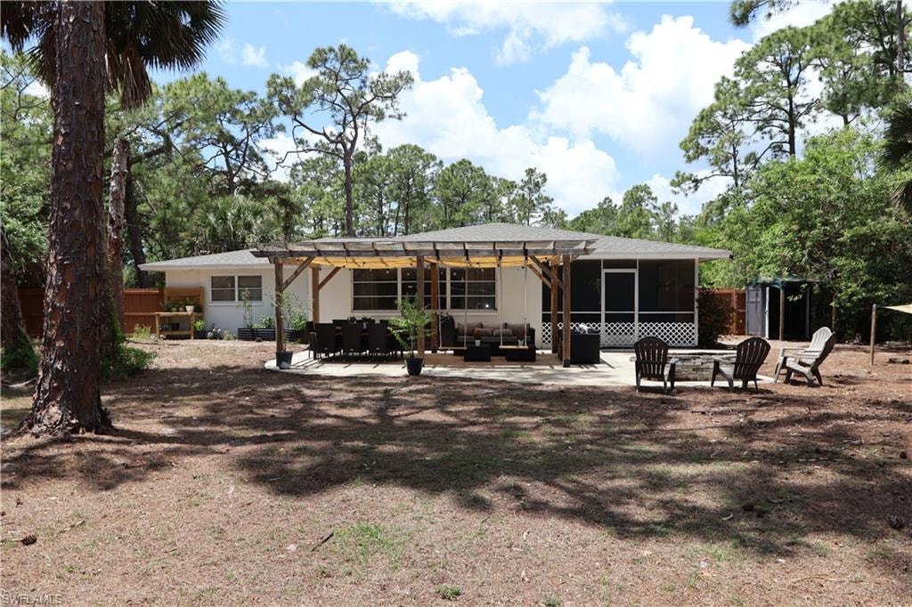 Expansive backyard featuring a concrete patio, a pergola structure, and mature trees