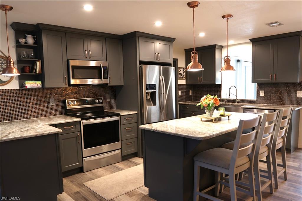 Kitchen featuring dark cabinetry, light-toned countertops, a mosaic tile backsplash, stainless steel appliances, and wood-finish flooring