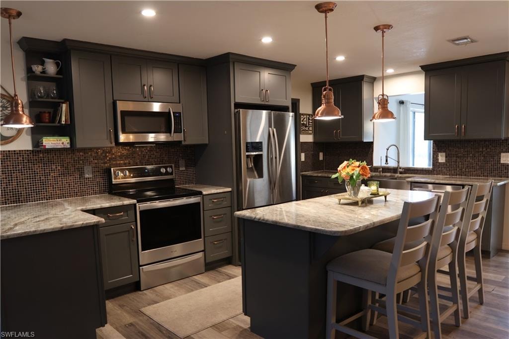 Kitchen featuring a central island with countertop seating, dark cabinetry, mosaic tile backsplash, and stainless steel appliances